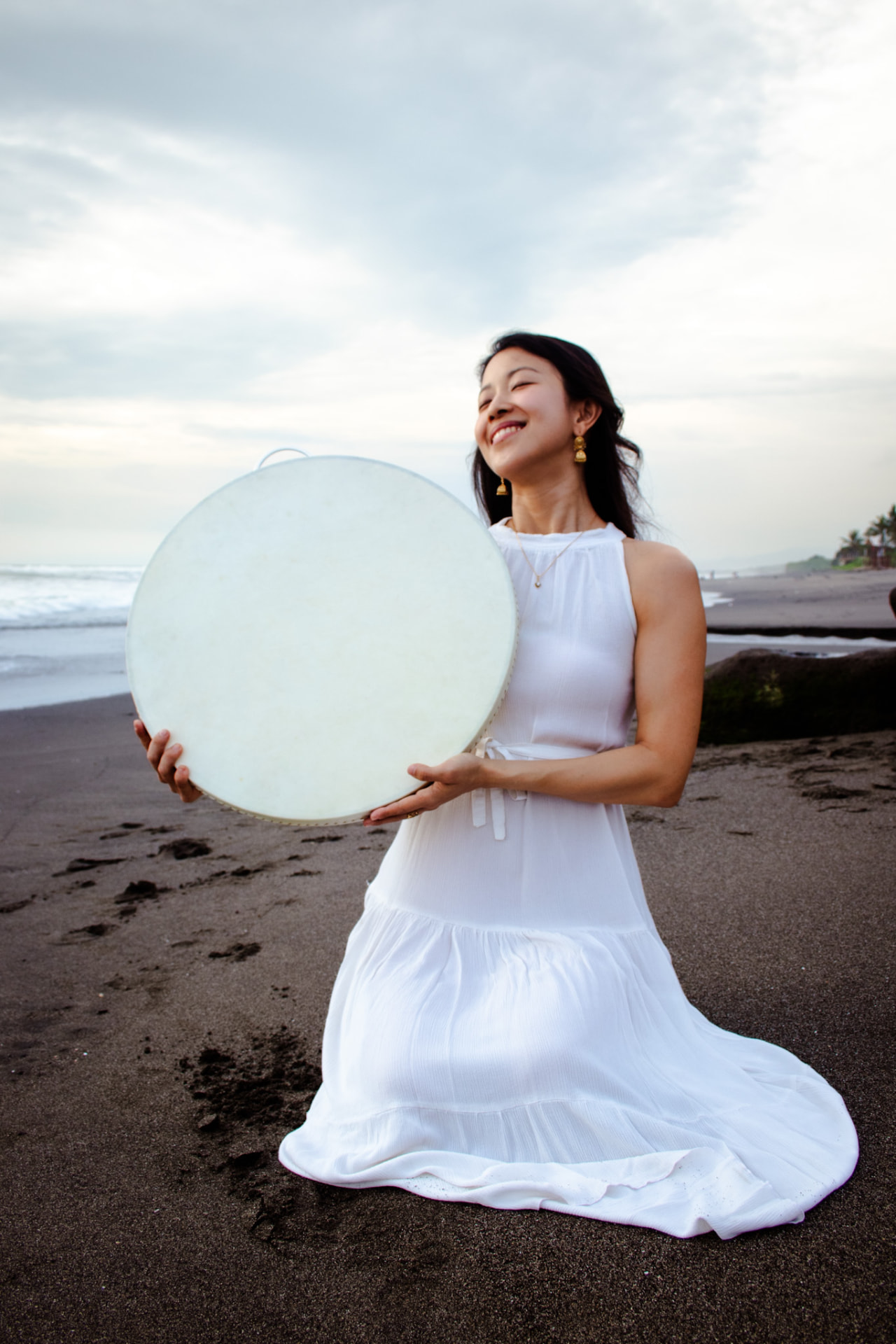 Diana holding a frame drum on a Bali beach