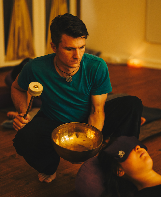 Dr Grant Smith holding a singing bowl above a resting participant