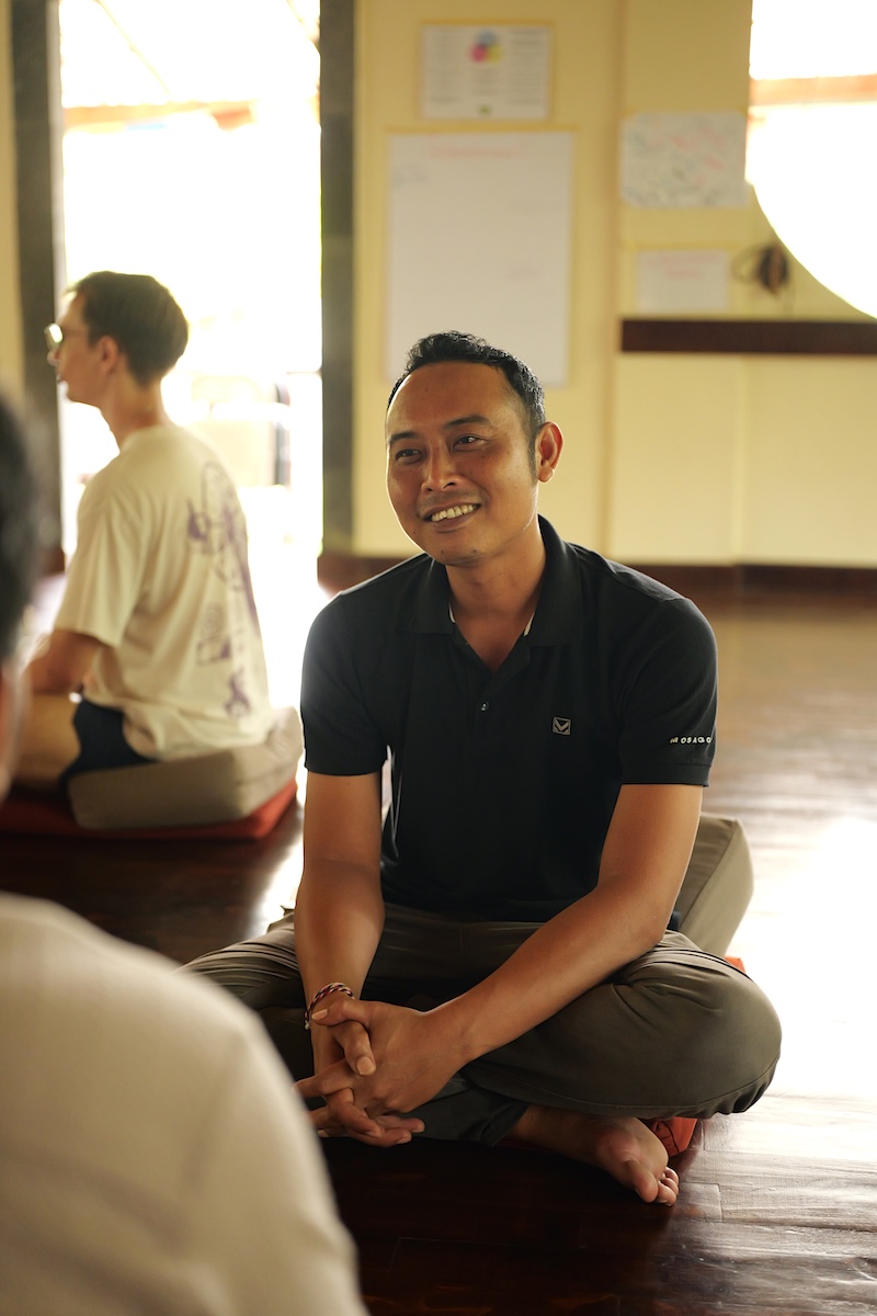 A Balinese facilitator smiling warmly in circle