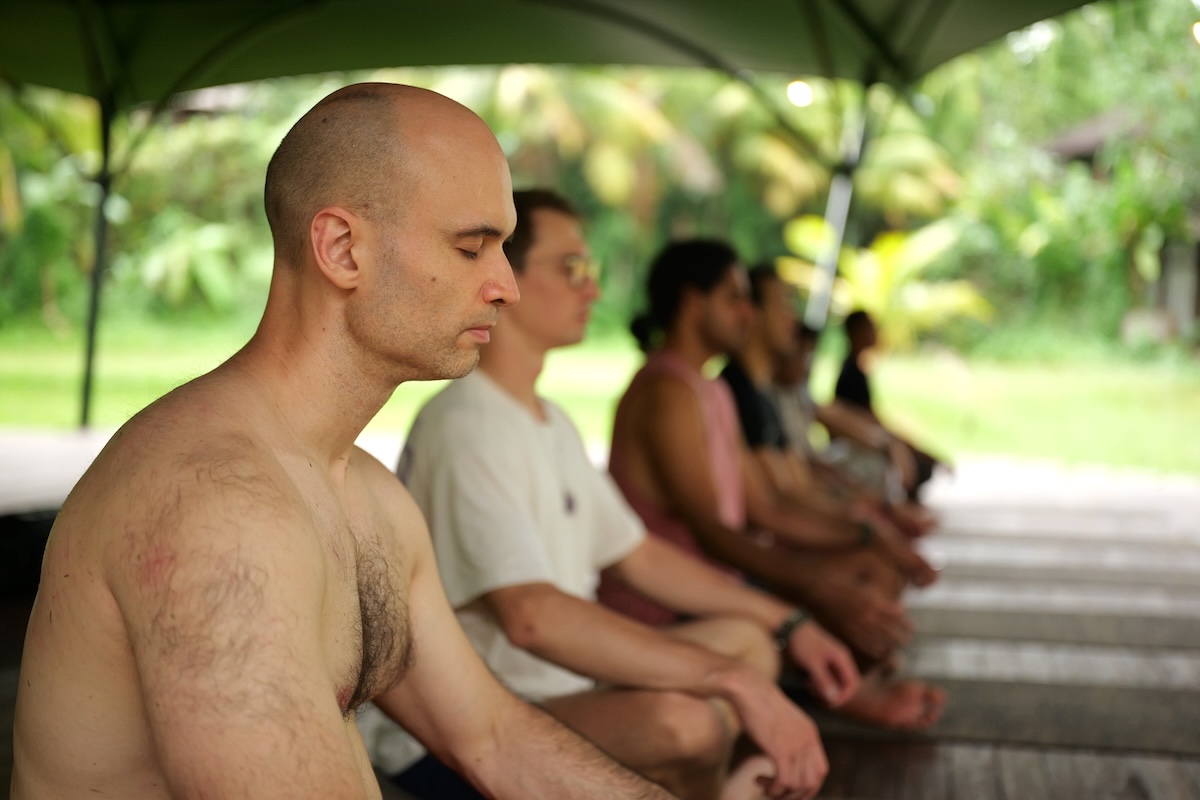 A line of men sitting in stillness with eyes closed